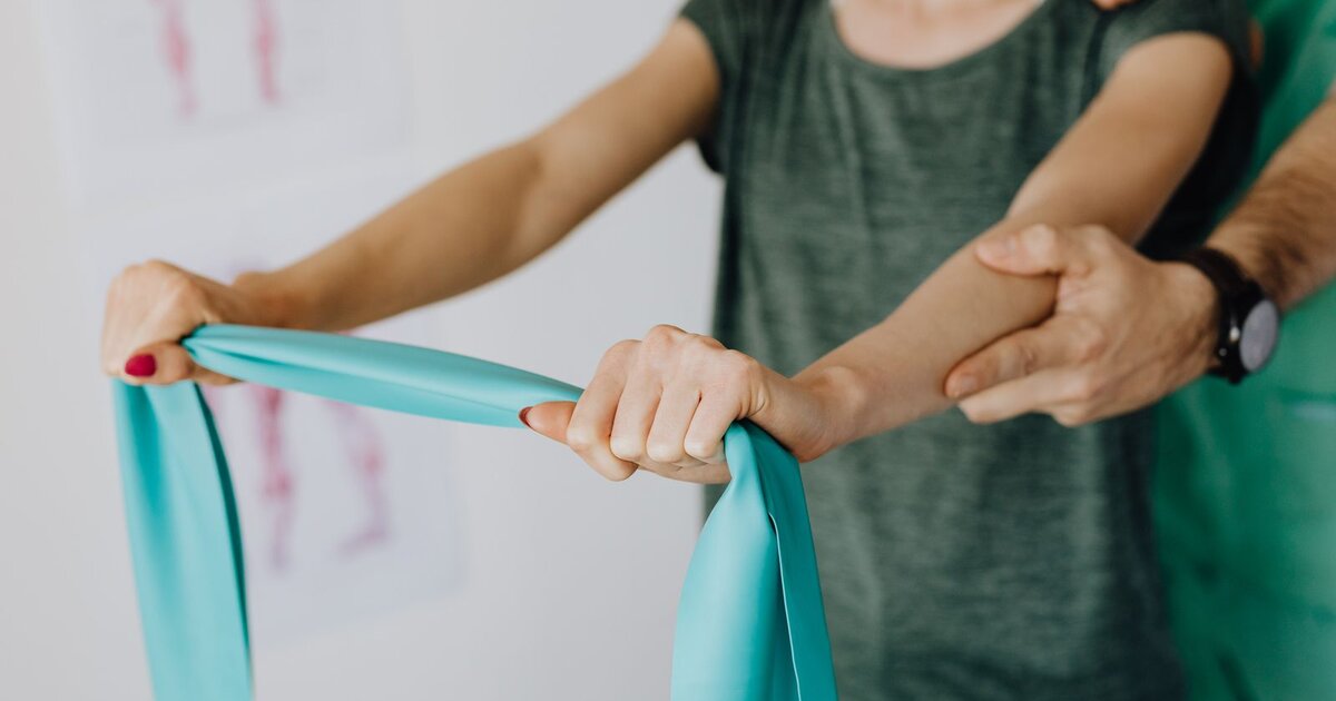 Physical therapist guiding a patient through a resistance band exercise in a clinic