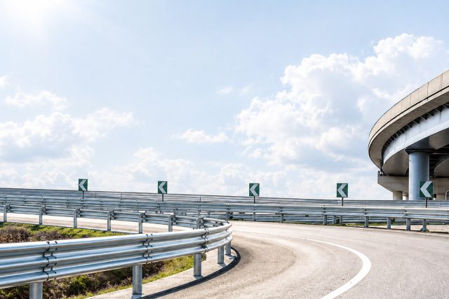 Metal guardrails curving along an empty highway under a pale hazy sky